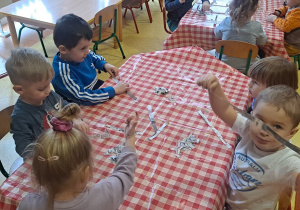 dzieci przy stolikach drą paski z gazet na mniejsze kawałeczki