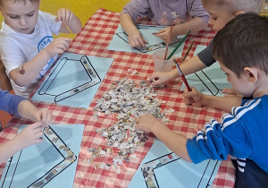 dzieci przygotowanymi kawałkami gazet wyklejają szablon karmnika dla ptaków