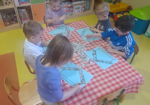 dzieci przygotowanymi kawałkami gazet wyklejają szablon karmnika dla ptaków