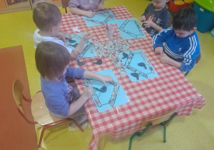 dzieci przygotowanymi kawałkami gazet wyklejają szablon karmnika oraz doklejają ptaki