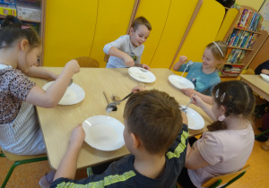 dzieci przy stolikach badały ciecz newtonowską i przenoszą ją łyżkami