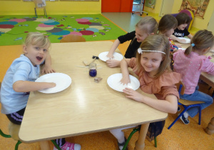 dzieci przy stolikach badały ciecz newtonowską i starają się ją przenieść w dłoniach