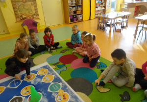 dzieci siedzą na dywanie w koło planszy