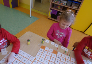 dzieci siedzą przy stolikach wykonują działania matematyczne na patyczkach