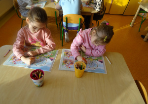dzieci przy stolikach kredkami uzupełniają karty pracy w książkach
