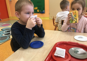 dzieci siedzą przy stolikach starają się dopasować torebkę kawy lub herbaty z odpowiednim pudełkiem