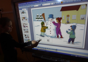 Dziewczynka pisakiem zaznacza na ekranie interaktywnym odpowiedz czy dane sytuacje na obrazkach są bezpieczne