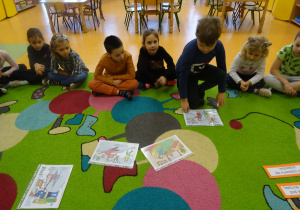 dzieci siedzą na dywanie, chłopiec przygląda się ilustracją dotyczącym zimy
