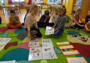 dzieci dopasowują ilustracje do opisów na karteczkach na dywanie