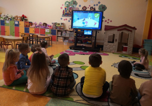 dzieci siedzą po turecku i w uwaga oglądają film edukacyjny o zabawie blisko jezdni