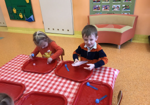 dzieci przy stolikach z bliska obserwują i dotykają kostki lodu