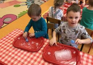 dzieci przy stolikach z bliska obserwują i dotykają bryły śniegu