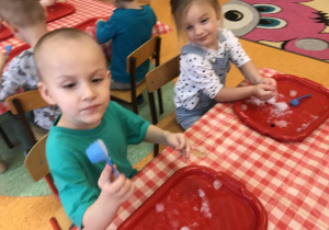 dzieci przy stolikach z bliska obserwują i dotykają bryły śniegu, starają się robić babeczki ze śniegu