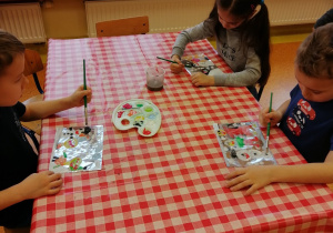dzieci przy stoliku malują farbami po foli aluminiowej obrazek zimowy