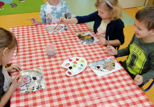 dzieci przy stoliku malują farbami po foli aluminiowej obrazek zimowy
