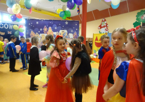 dzieci w strojach karnawałowych tańczą w parach trzymając między sobą napompowany balon