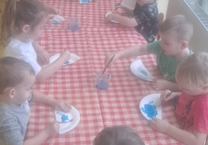 dzieci przy stolikach farbami malowały na niebiesko tyłów Papugi