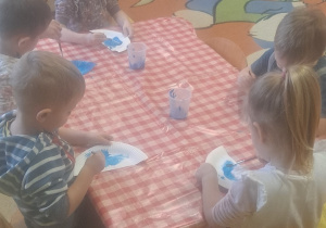 dzieci przy stolikach farbami malowały na niebiesko tyłów Papugi