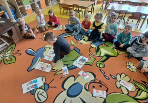 grupa układa na dywanie puzzle z rozsypanki kilku ilustracji