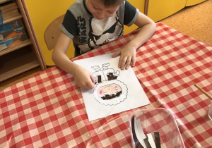 chłopiec po stoliku wykleja kawałkami papierów kolorowych postać Eskimosa