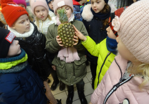 dzieci stoją w sklepie i trzymają ananasa