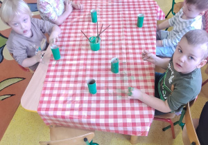 dzieci przy stolikach malowały zieloną farbą rolki po papierze toaletowym