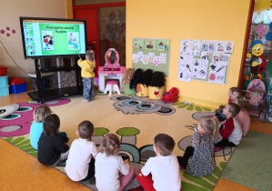 dzieci siedzą na dywanie oglądają prezentacje multimedialną o zawodzie fryzjera
