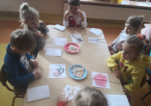 dzieci układają puzzle przy stolikach, na patyczkach wskazują ilość sylab danego wyrazu