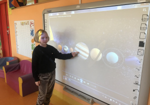 dziewczynka wskazuje na prezentacji multimedialnej planetę wskazaną przez nauczyciela