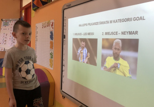 Szymon prezentuje dzieciom prezentacje multimedialną o piłkarzach