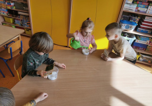 dzieci przy stolikach sieją rzeżuchę na wacie w plastikowych pojemnikach
