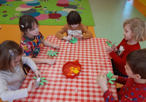 dzieci przy stolikach sklejają zielone gałązki