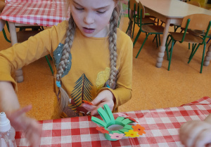 dziewczynka przy stoliku z dużym skupieniem przykleja na końcach gałązek kolorowe kwiaty z papieru