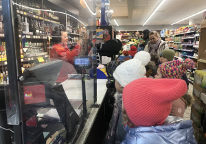 dzieci stoją przy kasie w sklepie spożywczym i obserwują jak wygląda praca kasjerki