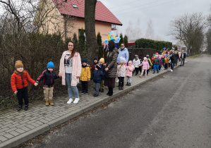 przedszkolaki w parach maszerują, niesioną jest Marzanna, Pani Wiosna oraz kolorowy krzak