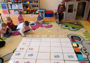 grupa na dywanie układa na planszy do kodowania według kodu kwiaty, zwracając uwagę na kolor oraz liczbę kropek w środku