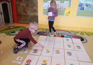 grupa na dywanie układa na planszy do kodowania według kodu kwiaty, zwracając uwagę na kolor oraz liczbę kropek w środku