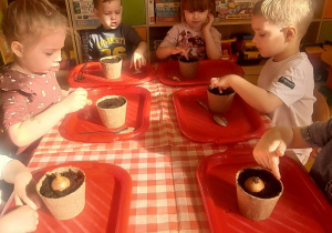 dzieci przy stolikach sadzą nasiona i cebule przygotowane przez panią, każdy ma swoją doniczkę