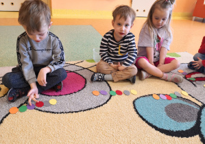 dzieci na dywanie układają kolorowe kropki według poleceń nauczyciela
