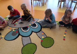 dzieci na dywanie układają kolorowe kropki według poleceń nauczyciela
