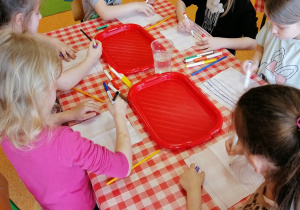 dzieci przy stolikach malują chusteczki higieniczne pisakami na różne kolory