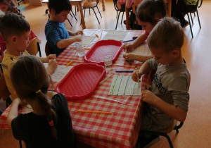 dzieci przy stolikach malują chusteczki higieniczne pisakami na różne kolory