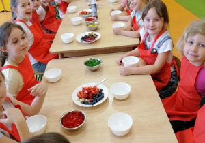 cała grupa siedzi przy stolikach przygotowują się do zrobienie deseru owocowego