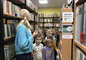 bibliotekarka oprowadza dzieci między regałami pokazuje zbiór książek