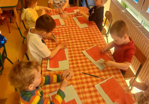 dzieci przy stolikach na niebieską kartkę przyklejają pięć czerwonych kwadratów wg polecenie nauczyciela