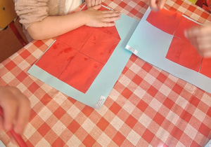 dzieci przy stolikach na niebieską kartkę przyklejają trójką czerwony wg polecenie nauczyciela
