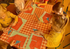 dzieci przy stolikach na niebieską kartkę przyklejają trójką niebieski wg polecenie nauczyciela
