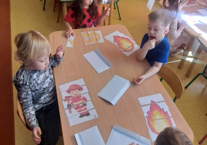 dzieci przy stolikach układają puzzle dotyczące pracy strażaka