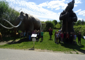 grupa dzieci na tle wielkiego mamuta oraz innej postaci