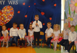 dzieci siedzą jedno z nich mówi wierszyk przez mikrofon